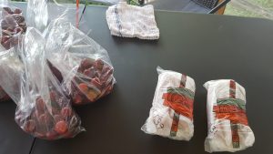 Packages of sausages and plums sit on a table.