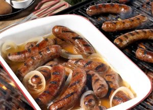 Bratwursts sitting in a hot tub of beer and onions on the barbecue grill