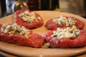 Burgers being stuffed with blue cheese crumbles for the barbecue