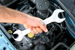 hand holding a wrench over a car engine