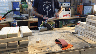 Sanding the Jenga pieces on a belt sander clamped to a work bench